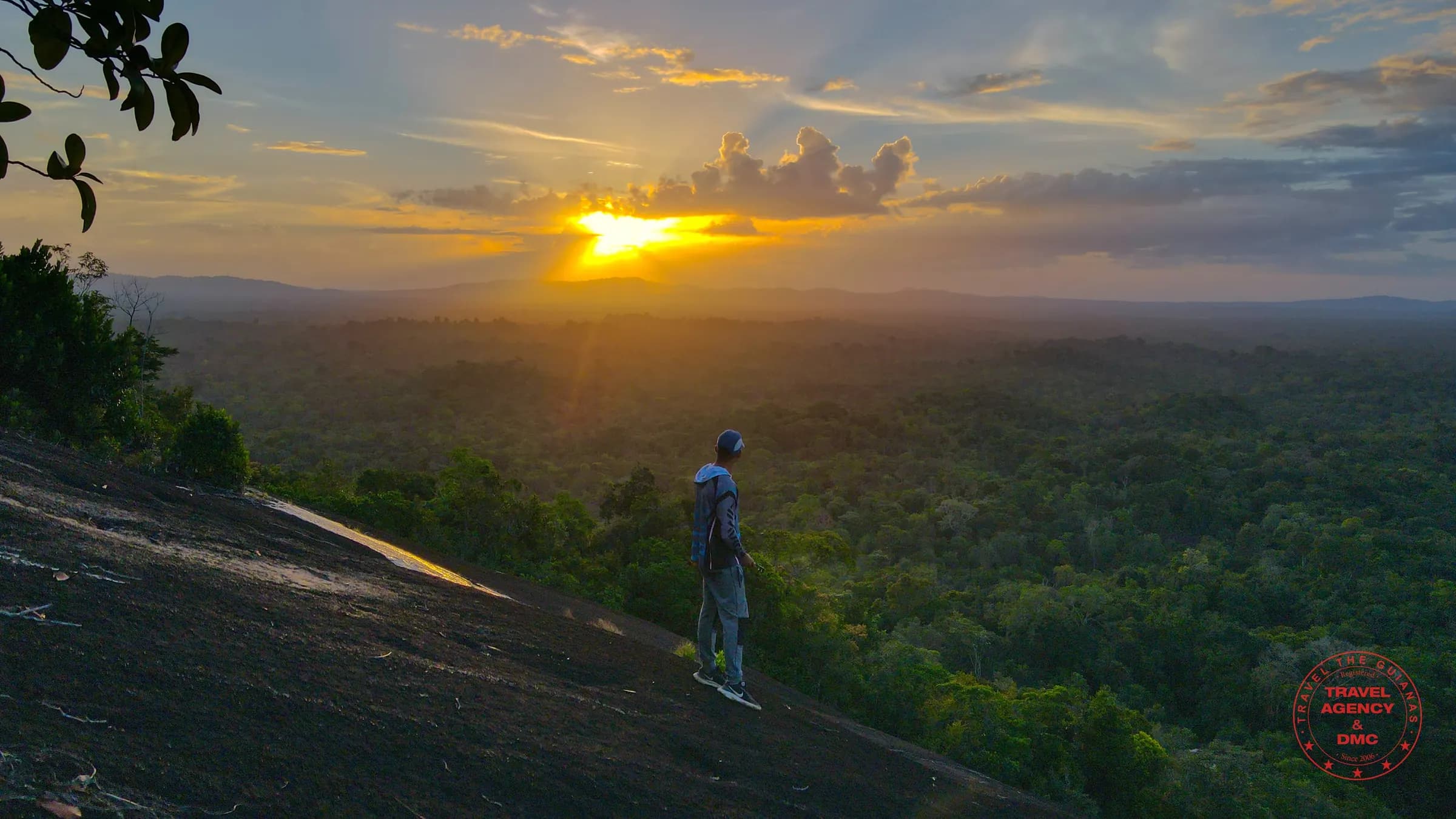 A hiker on the granite dome of Fredberg above the Suriname rainforest at sunset